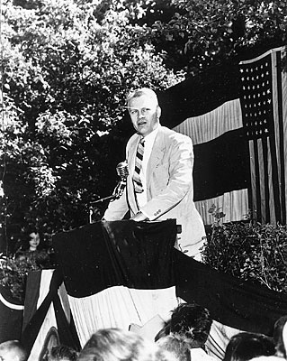 Congressman Gerald R. Ford speaking from a bunting-draped platform at a Fourth of July celebration in 1950, a crowd in the foreground
